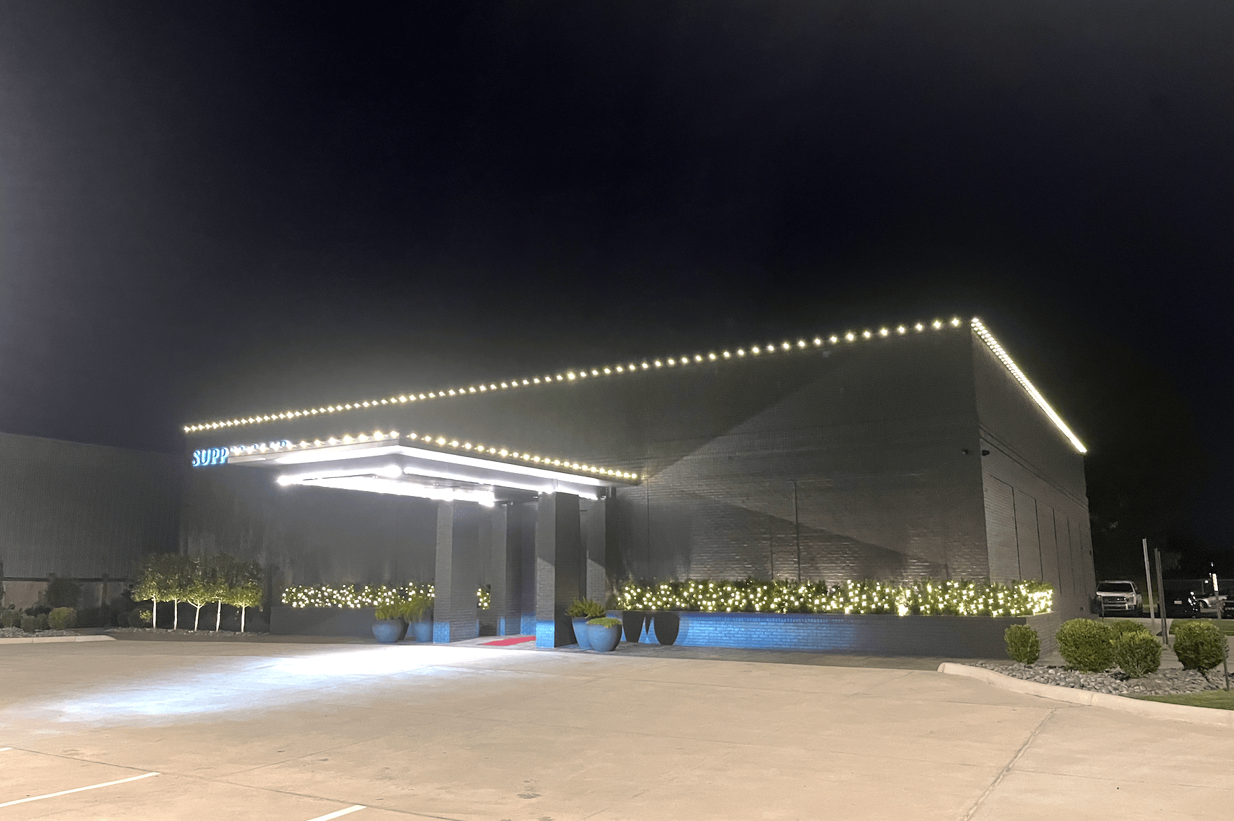 Commercial Christmas lighting installation along a storefront roofline and hedges