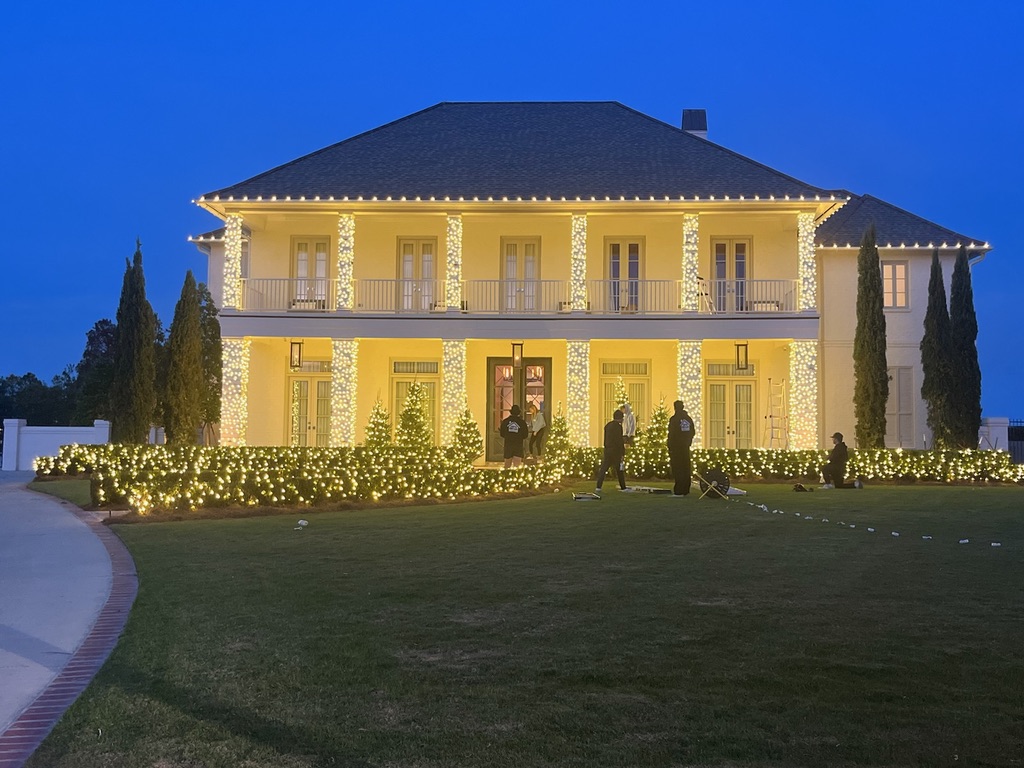 Crew installing warm-white Christmas lights on a columned house