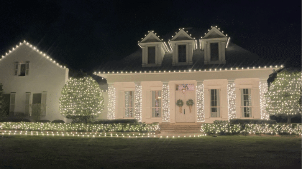 Warm-white Christmas lighting on a two-story house: roofline, wrapped columns, and landscape